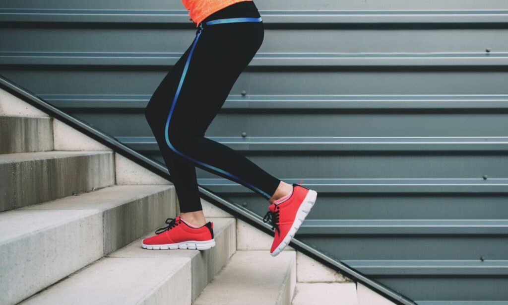 daily exercise -Person in athletic leggings and red sneakers climbing concrete stairs outdoors