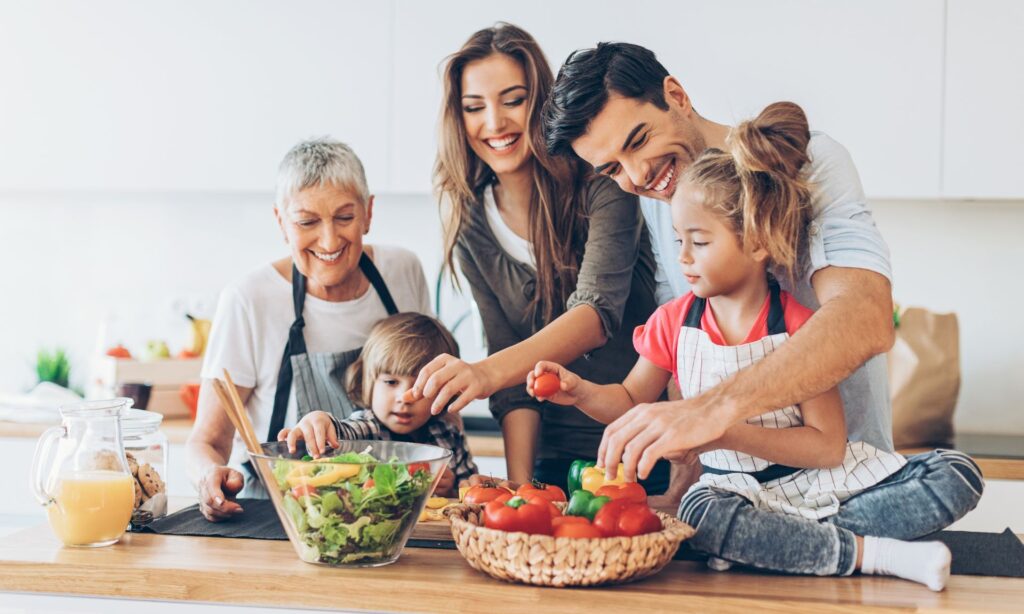 A happy family of different generations preparing a meal together in the kitchen, with children reaching for fresh vegetables and adults smiling