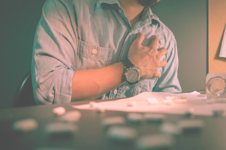 lower the risk of heart attack - A close-up shot of a tired office worker holding his chest, appearing distressed, symbolizing the physical strain and stress of working overtime.