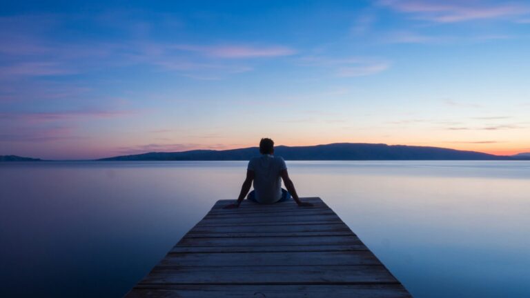 Person sitting alone at the end of a wooden dock overlooking a still lake at sunset, symbolizing the quiet moments before anger strikes.