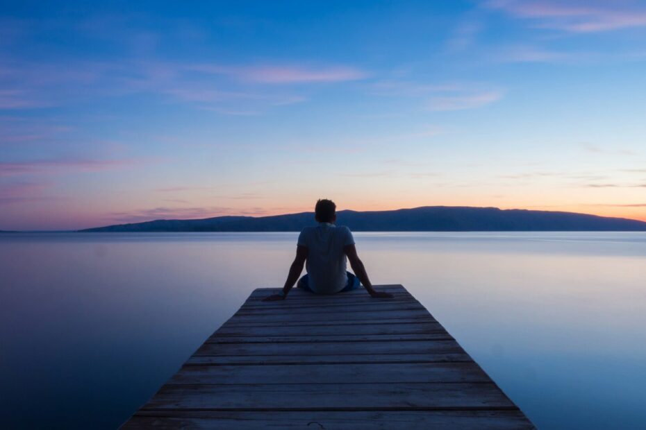 Person sitting alone at the end of a wooden dock overlooking a still lake at sunset, symbolizing the quiet moments before anger strikes.