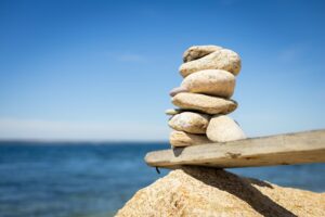 A stack of smooth stones balanced on a rock near the ocean, symbolizing mindfulness, stability, and ways to stay balanced in life.