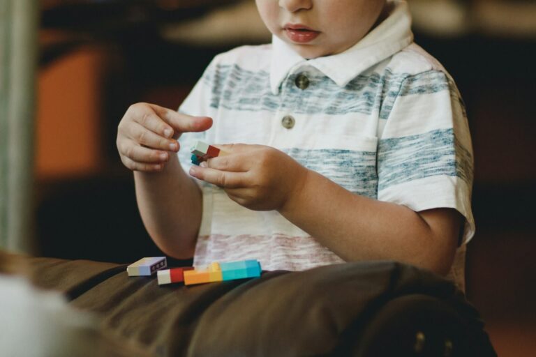 Child holding colorful building blocks and focusing intently on play, representing the learning and development styles of children with autism.