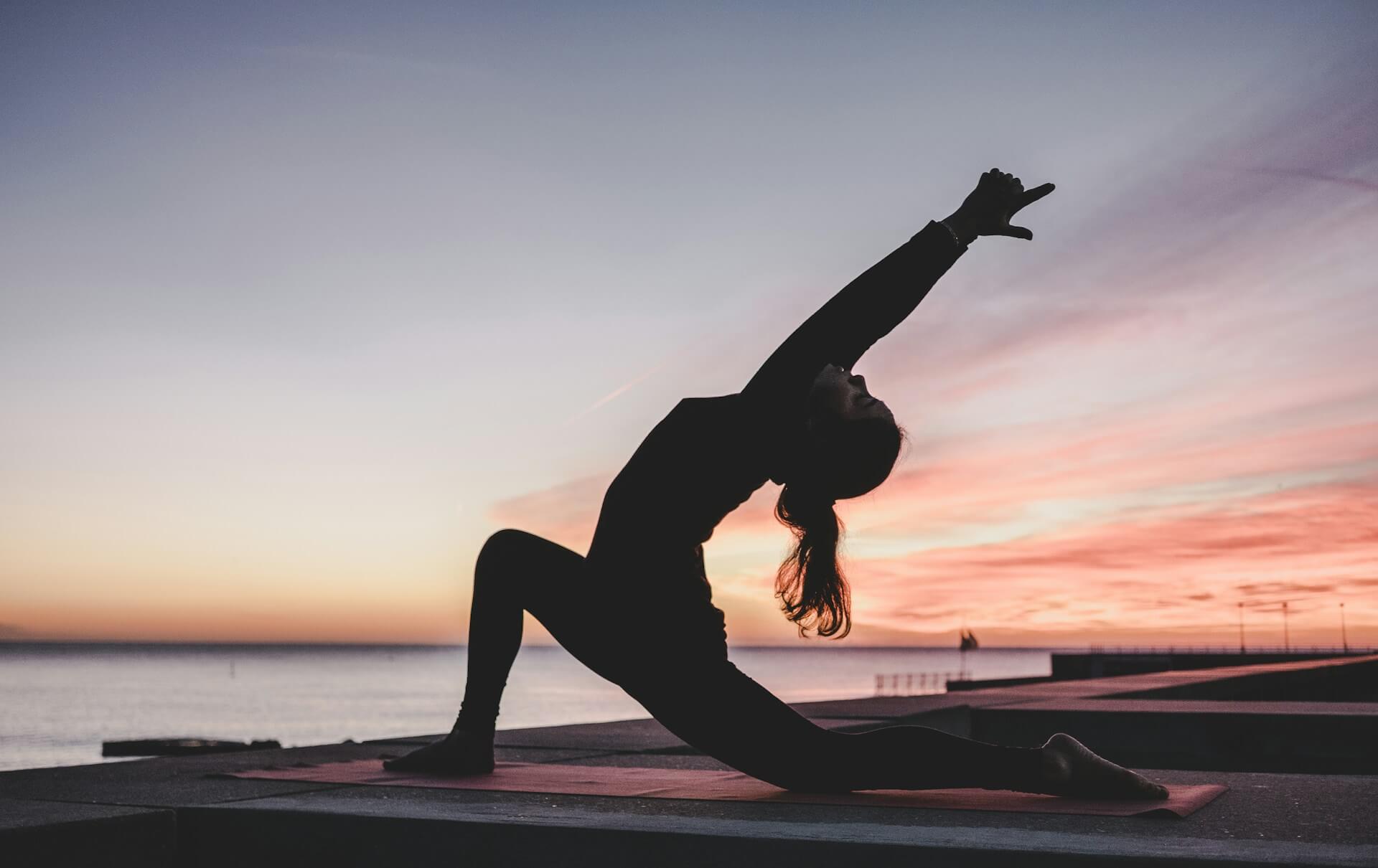 Person practicing yoga at sunrise, stretching in a deep lunge pose, symbolizing peaceful and intentional daily yoga rituals.