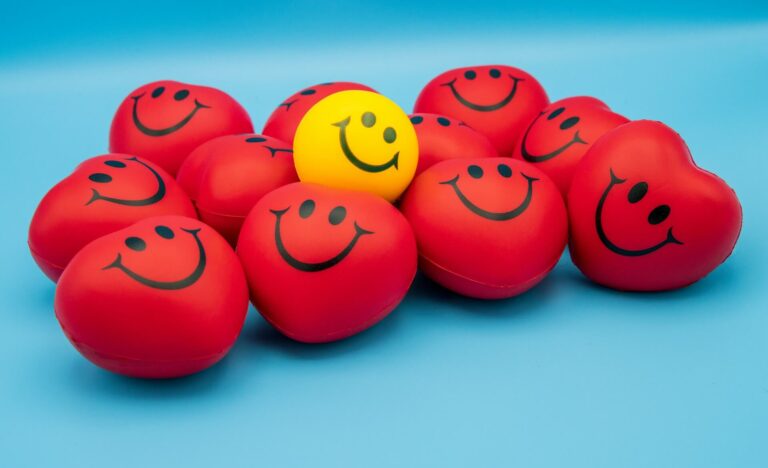 Group of red heart-shaped stress balls with smiling faces and one yellow smiley face in the center, symbolizing how depression symptoms can be hidden behind cheerful exteriors.