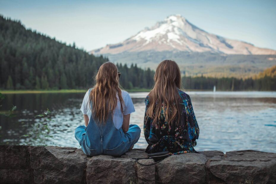 Two people sitting together on a stone ledge by a peaceful lake with mountains in the background, symbolizing companionship and support for someone living with depression.