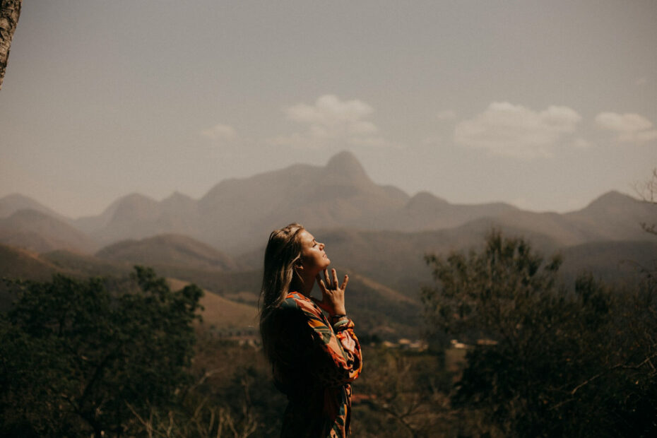 Person standing outdoors with eyes closed and hands gently raised near the face, practicing mindfulness and reflecting daily spiritual habits in a peaceful mountain landscape.