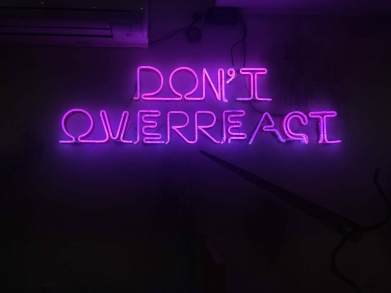 Neon purple sign reading don’t overreact symbolizing emotional control and overcoming overreacting