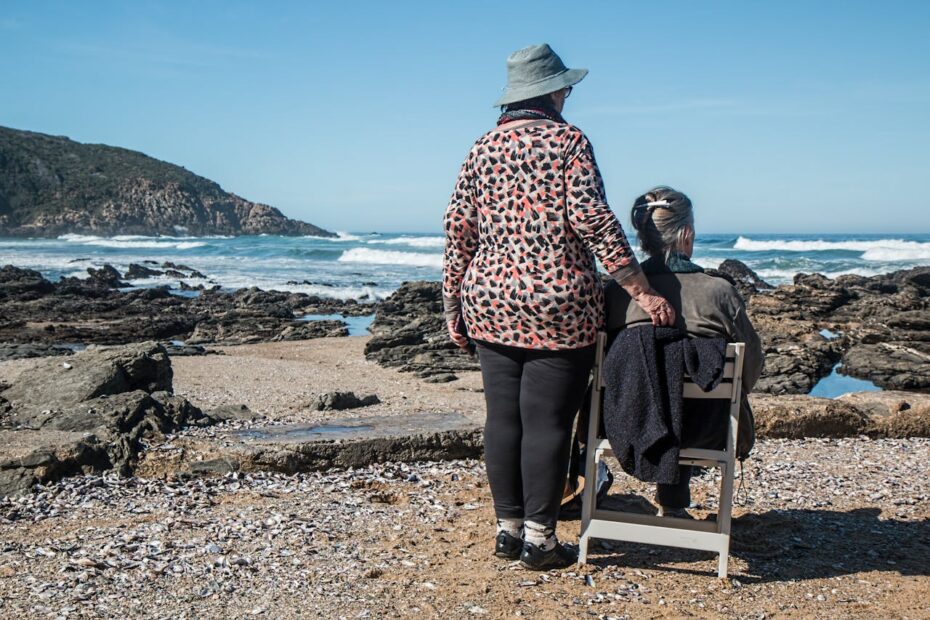 Two friends sitting and standing by a rocky beach looking at the ocean, reflecting how friendships change over time while sharing a quiet moment together.